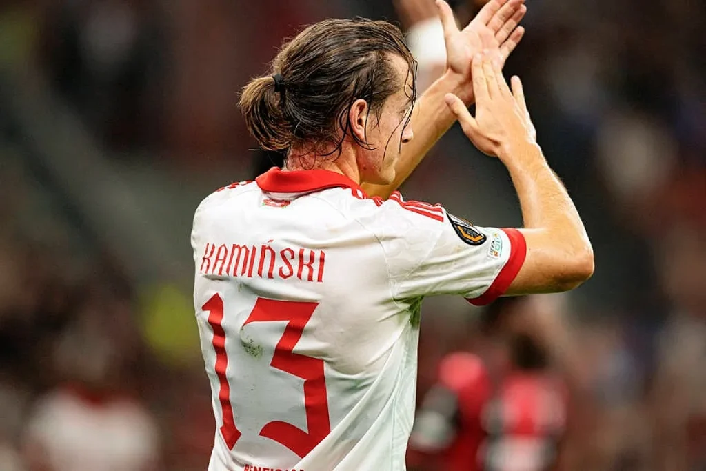 Jogador de costas com camisola branca e vermelha n.º 13 "Kaminski", a aplaudir o público em estádio