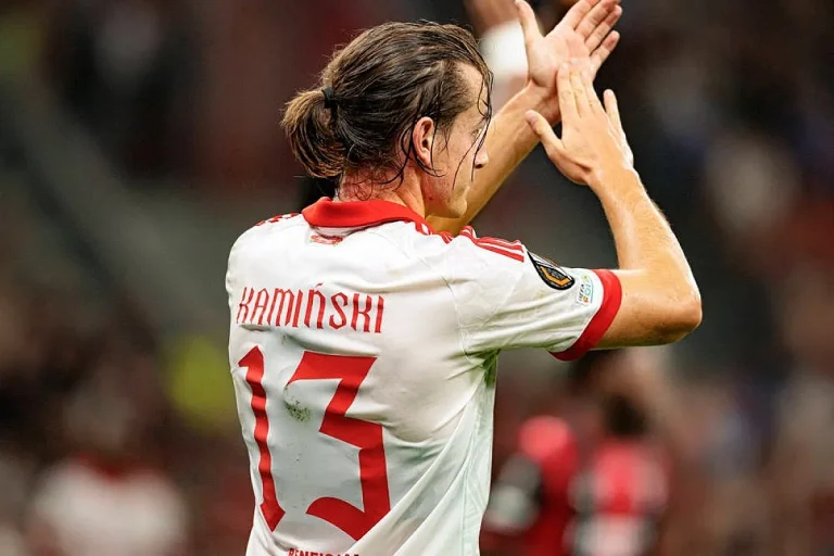 Jogador de costas com camisola branca e vermelha n.º 13 "Kaminski", a aplaudir o público em estádio