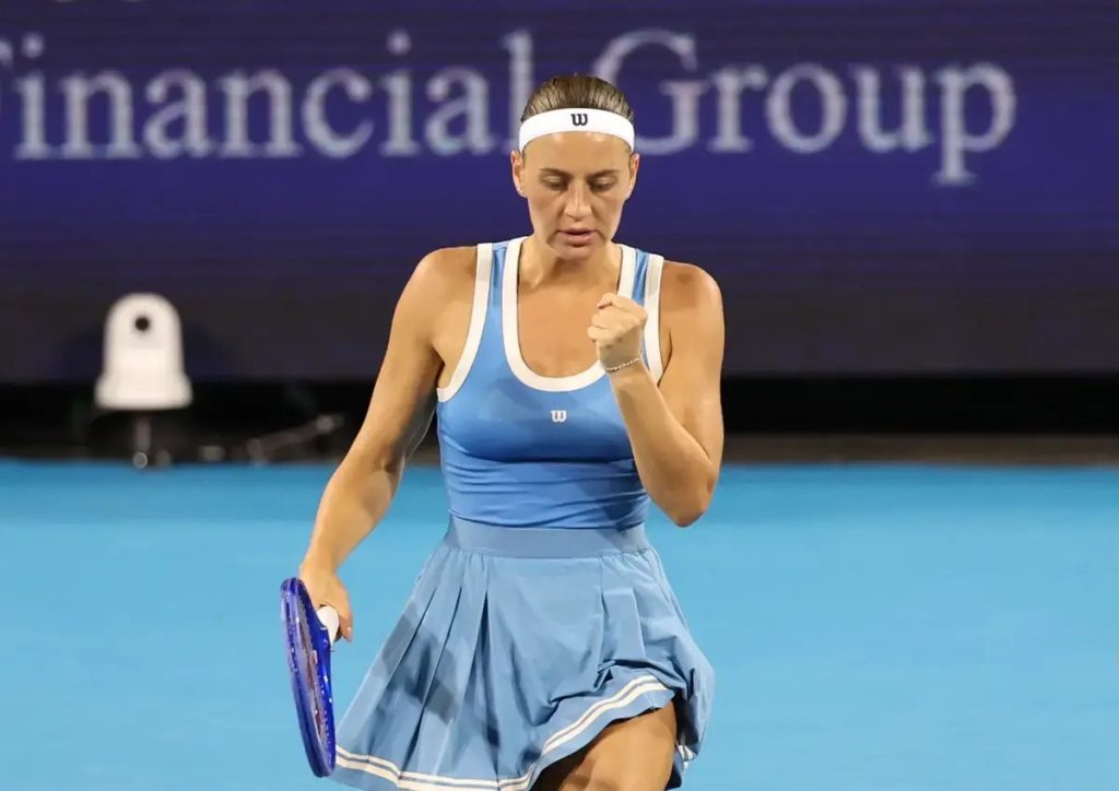 Tennis player in a blue Wilson dress and white headband clenches her fist on a blue court, racket in hand, Financial Group backdrop