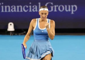 Tennis player in a blue Wilson dress and white headband clenches her fist on a blue court, racket in hand, Financial Group backdrop