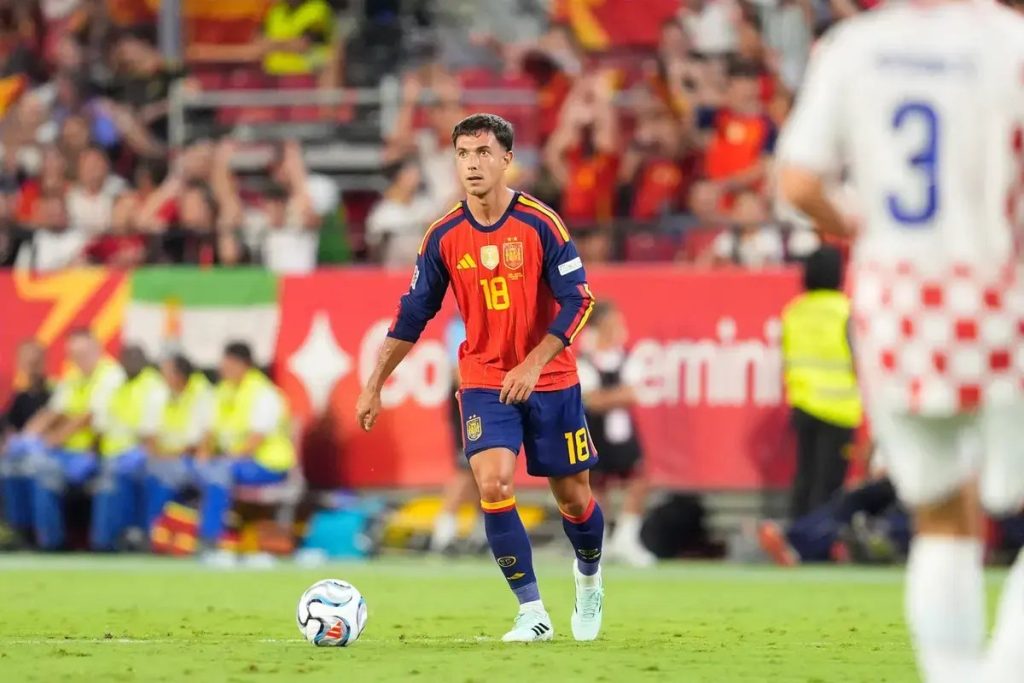 Spain midfielder in red No. 18 kit with the Spain crest passes the ball during a match, white-shirted Croatia player in foreground