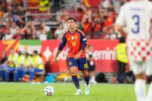Spain midfielder in red No. 18 kit with the Spain crest passes the ball during a match, white-shirted Croatia player in foreground