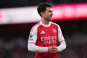 Footballer in red Arsenal home kit with Emirates sponsor, grimacing and clasping hands at the Emirates Stadium during a Premier League match.