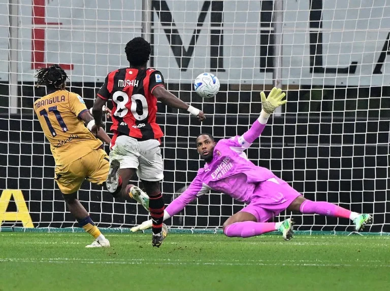 Jogador do Bologna n.º 11 remata à baliza, enquanto o defesa do AC Milan n.º 80 Musah e o guarda-redes de rosa tentam defender no San Siro.
