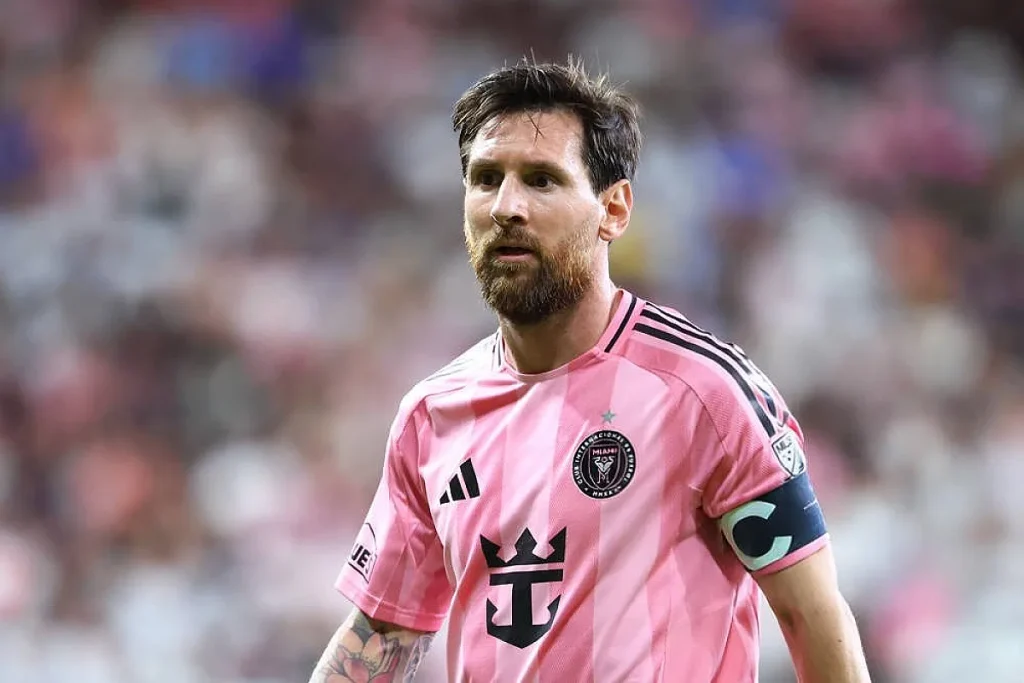 Jogador de camisola rosa do Inter Miami, com braçadeira de capitão, num estádio com público desfocado ao fundo.