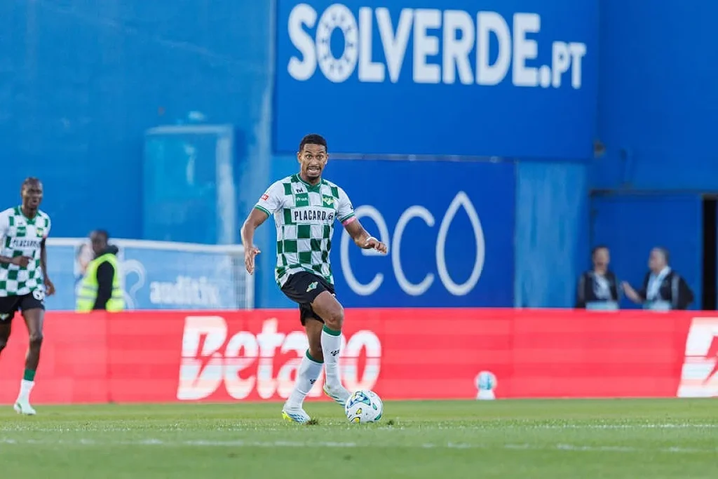 Jogador do Moreirense, de camisola verde e branca às quadrados, a conduzir a bola num jogo contra o Estrela da Amadora