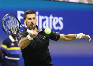Tennis player in black Lacoste shirt and white wristbands hitting a forehand near a blue Emirates sign; ball mid-air
