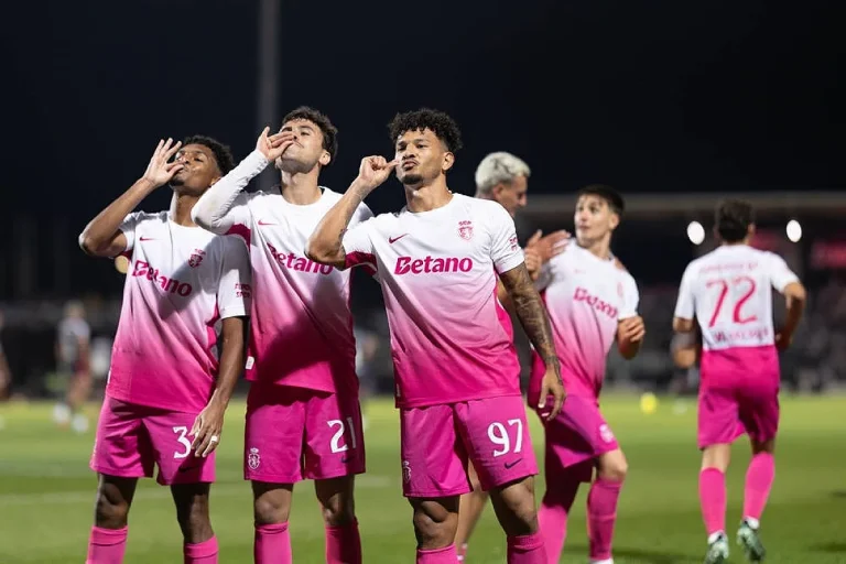 Jogadores do Casa Pia com camisola cor-de-rosa e Betano celebram um golo à noite, com o número 97 em destaque.