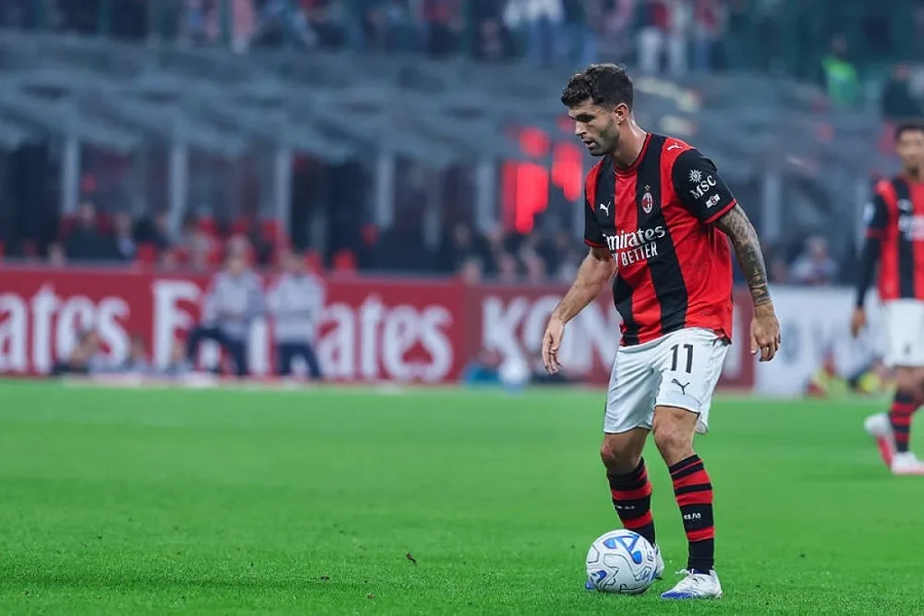 Jogador do AC Milan, de camisola n.º 11 listada a vermelho e preto, conduz a bola em campo durante um jogo.