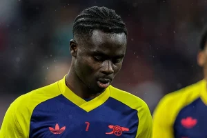 Jogador do Arsenal, de camisola amarela e azul com o número 7, cabisbaixo num estádio chuvoso durante o aquecimento.