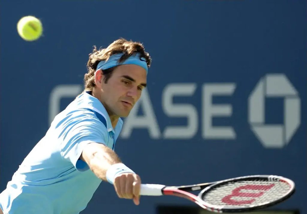 Tennis player in light blue shirt and headband hits a forehand return, ball in the air, Chase logo behind him