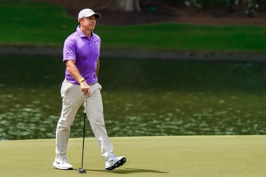 Golfer in purple polo and white cap putting on a green beside a pond, looking toward the hole. Matches the article on McIlroy's advice to take breaks.