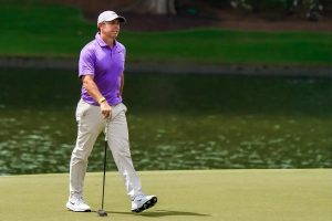 Golfer in purple polo and white cap putting on a green beside a pond, looking toward the hole. Matches the article on McIlroy's advice to take breaks.