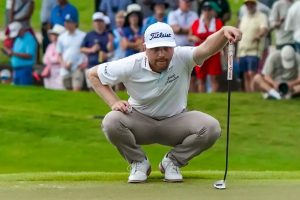 Golfer in white Titleist cap and Hall of Fame-style white polo crouches to read a putt on a green, with spectators behind. Ryan Gerard, Titleist sponsored.