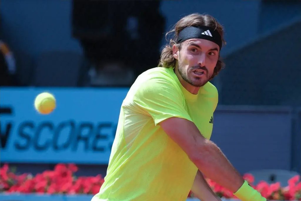 Tennis player in neon yellow shirt and black headband mid-swing on a clay court, ball in motion beside him, blue sponsor banner behind