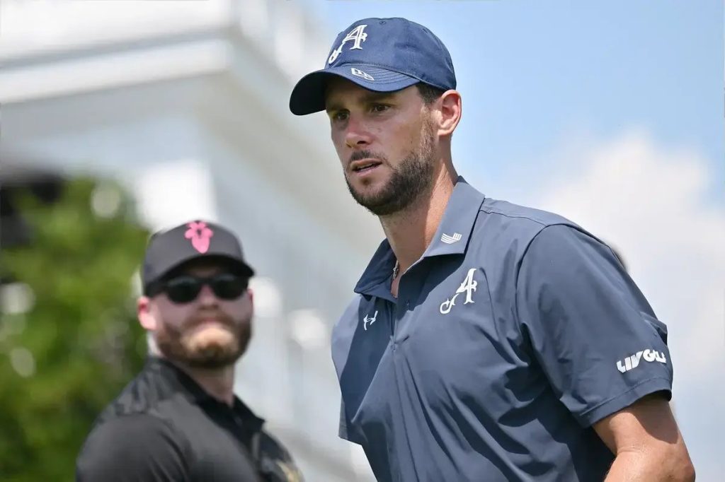 Golfer in navy cap and LIV Golf polo at a tournament, with a security staffer in sunglasses behind him