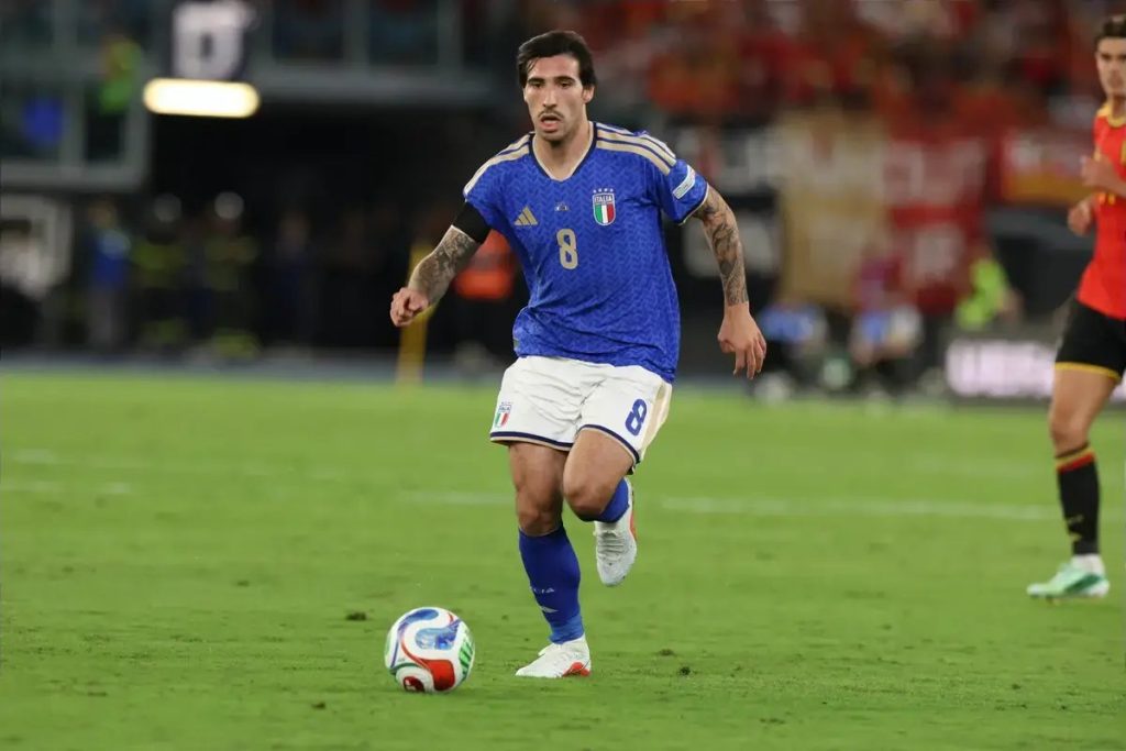 Footballer wearing Italy's blue No. 8 kit dribbling the ball on the pitch during a match against Belgium, Nations League.